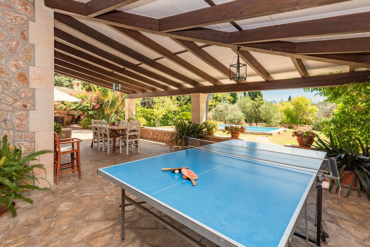 Covered terrace with table tennis setup and outdoor dining area, surrounded by lush gardens.