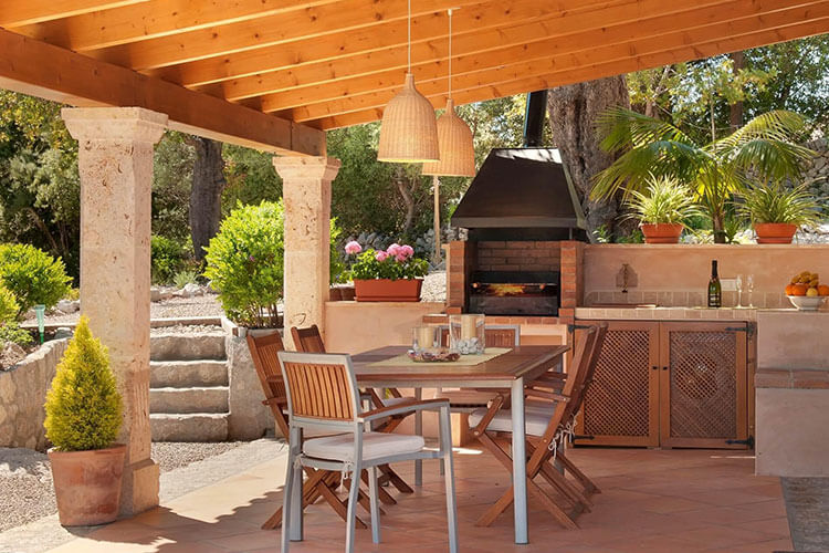 Charming covered outdoor kitchen and dining area with barbecue, rustic columns, and Mediterranean garden views.
